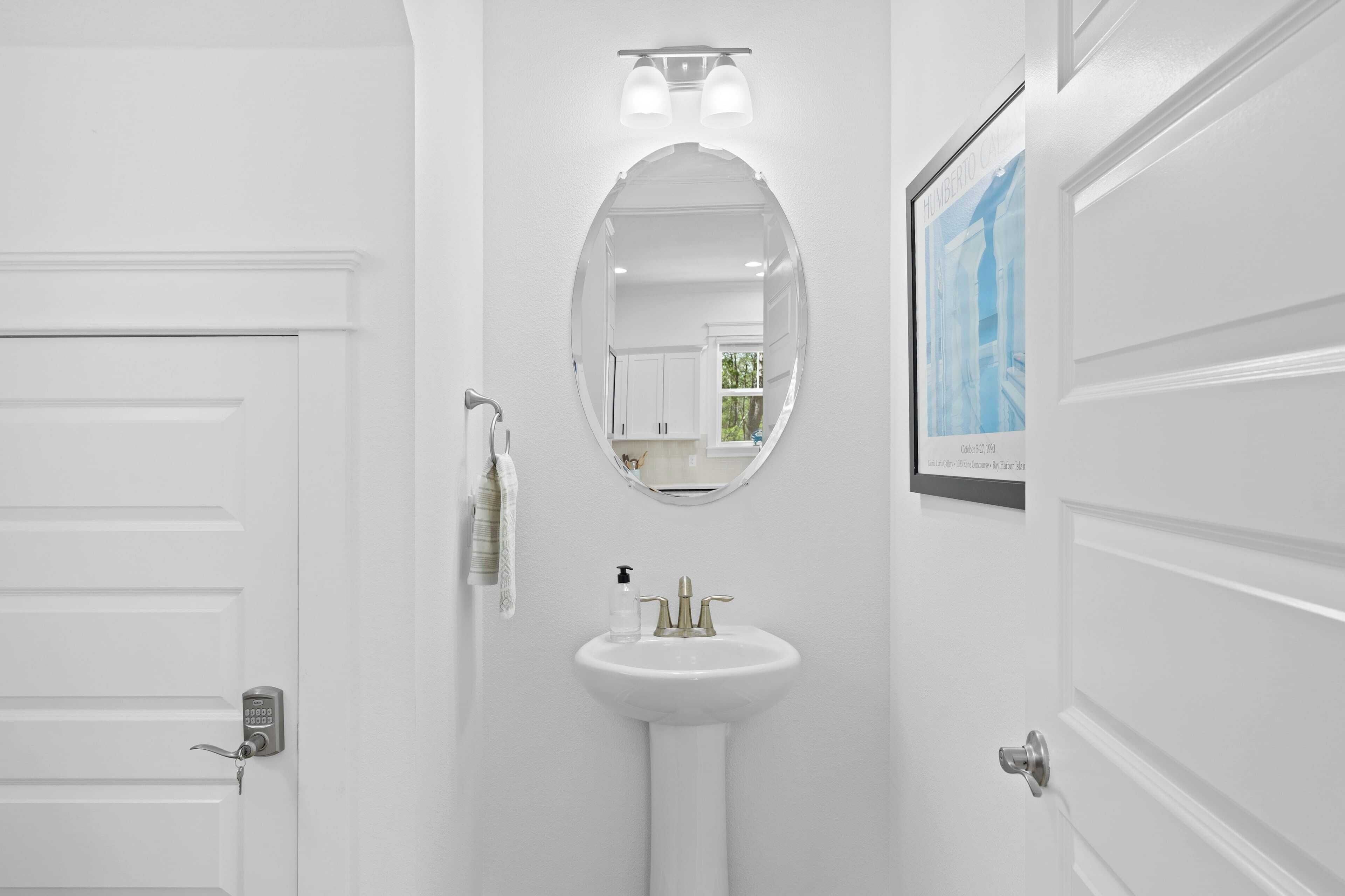 Een badkamer met een witte deur, een ronde spiegel, een wastafel op een zuil en een ingelijste foto aan de muur.