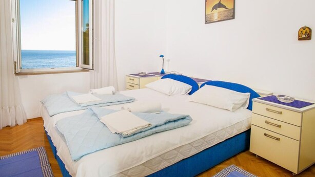 A bedroom with a large bed, a nightstand, a bedside table, a window with a view of the sea, and a painting on the wall. - Comfortable Stay with Sea View in Petrovac - One Bedroom Apartment 3 (Petrovac na Moru)