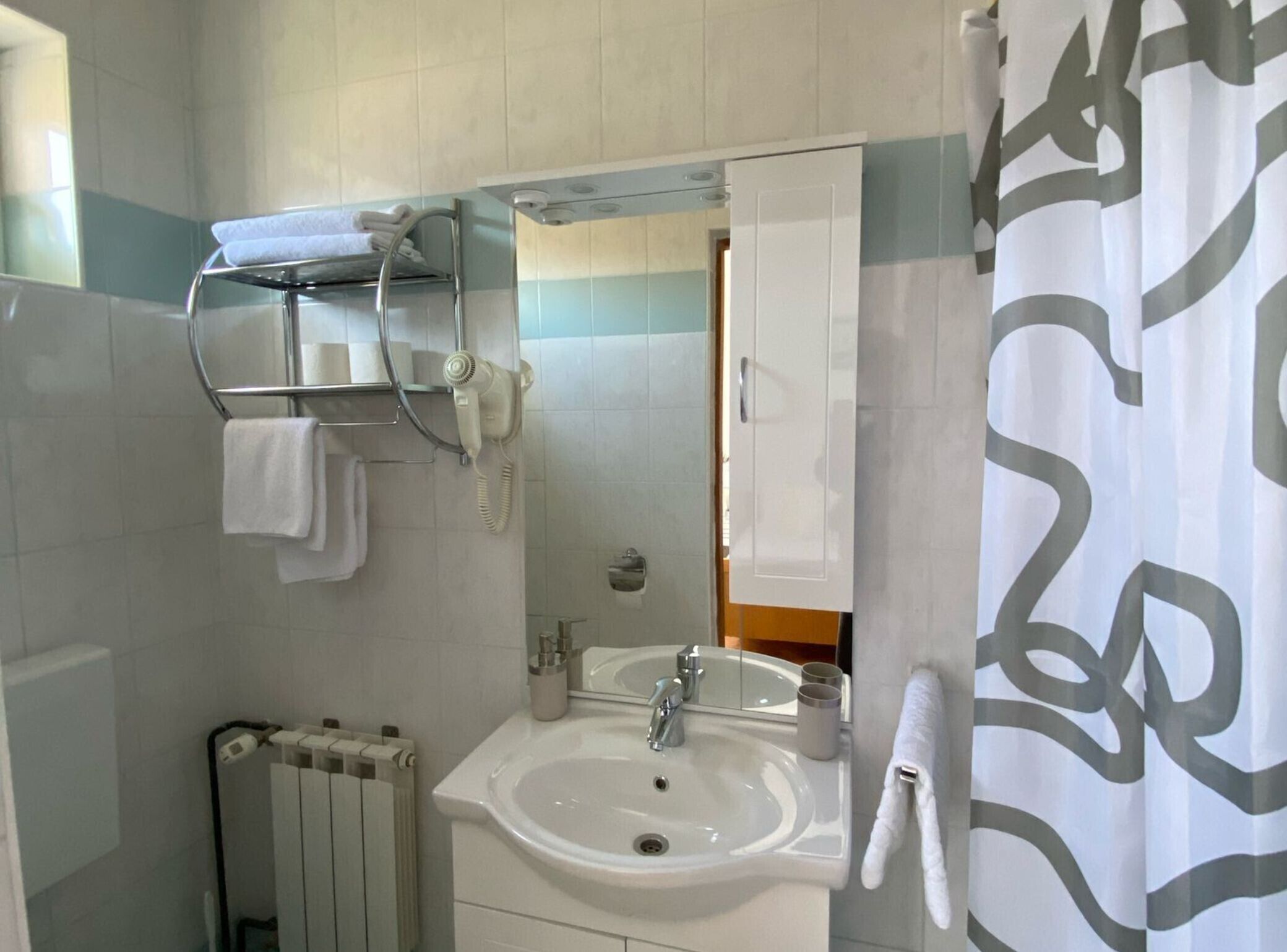 Une salle de bain avec un lavabo blanc, un miroir, un porte-serviettes, un radiateur et un rideau de douche.