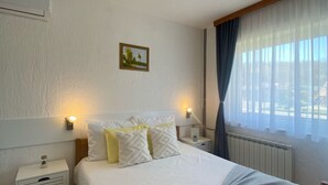 Ett hotellrum med en säng, två sängbord, ett litet bord, en tavla på väggen och ett fönster med gardiner.