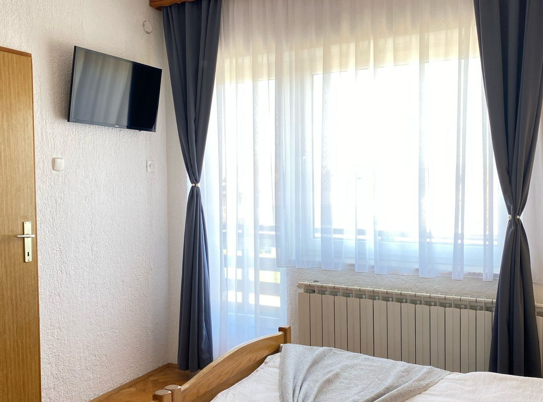 Quarto com cama, televisão na parede e janela com cortinas.