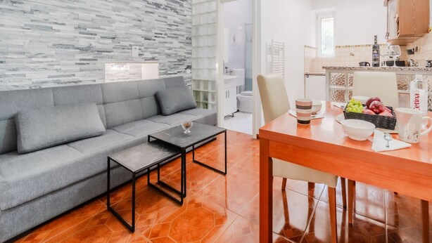 A modern living room with a grey sofa, a small black coffee table, and a wooden dining table with a bowl of fruit and a cup. - Urban Nest Apartment - Apartment (Zagreb)