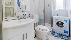 A modern bathroom with a sink, toilet, shower, and washing machine. - Urban Nest Apartment - Apartment (Zagreb)