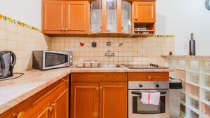 A compact kitchen with wooden cabinets, a microwave, a kettle, a toaster, a sink, and an oven. - Urban Nest Apartment - Apartment (Zagreb)
