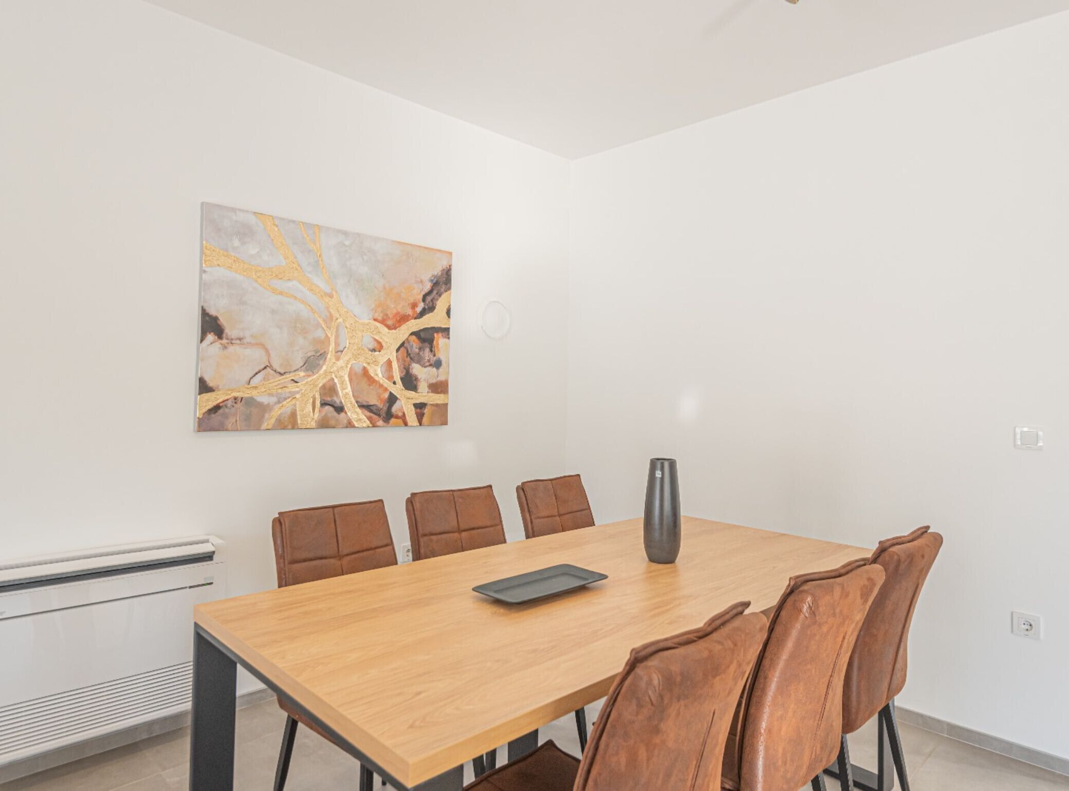 Een vergaderruimte met een houten tafel, zes bruine leren stoelen, een grijze vaas en een groot abstract schilderij aan de muur.