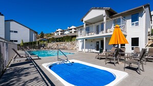 A rectangular swimming pool with a diving board, surrounded by lounge chairs and umbrellas. - Mountain View Retreat - Condo in Chelan (Chelan)