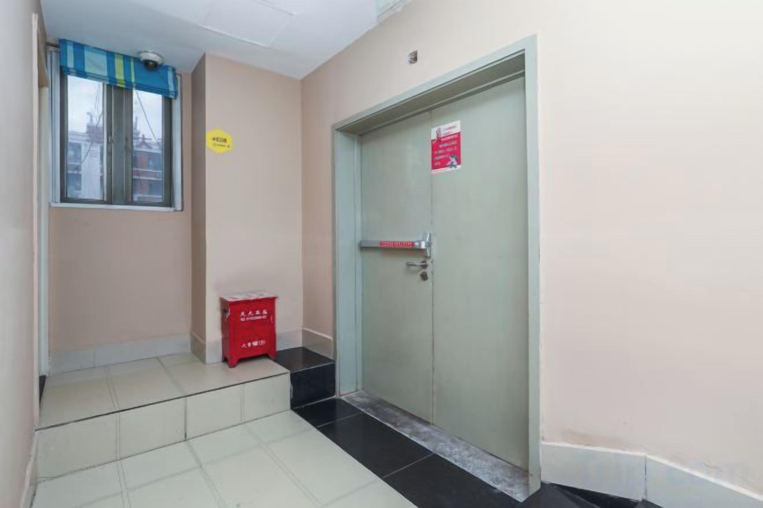 A hallway with a door, a window with a blue blind, and a red box on the floor.