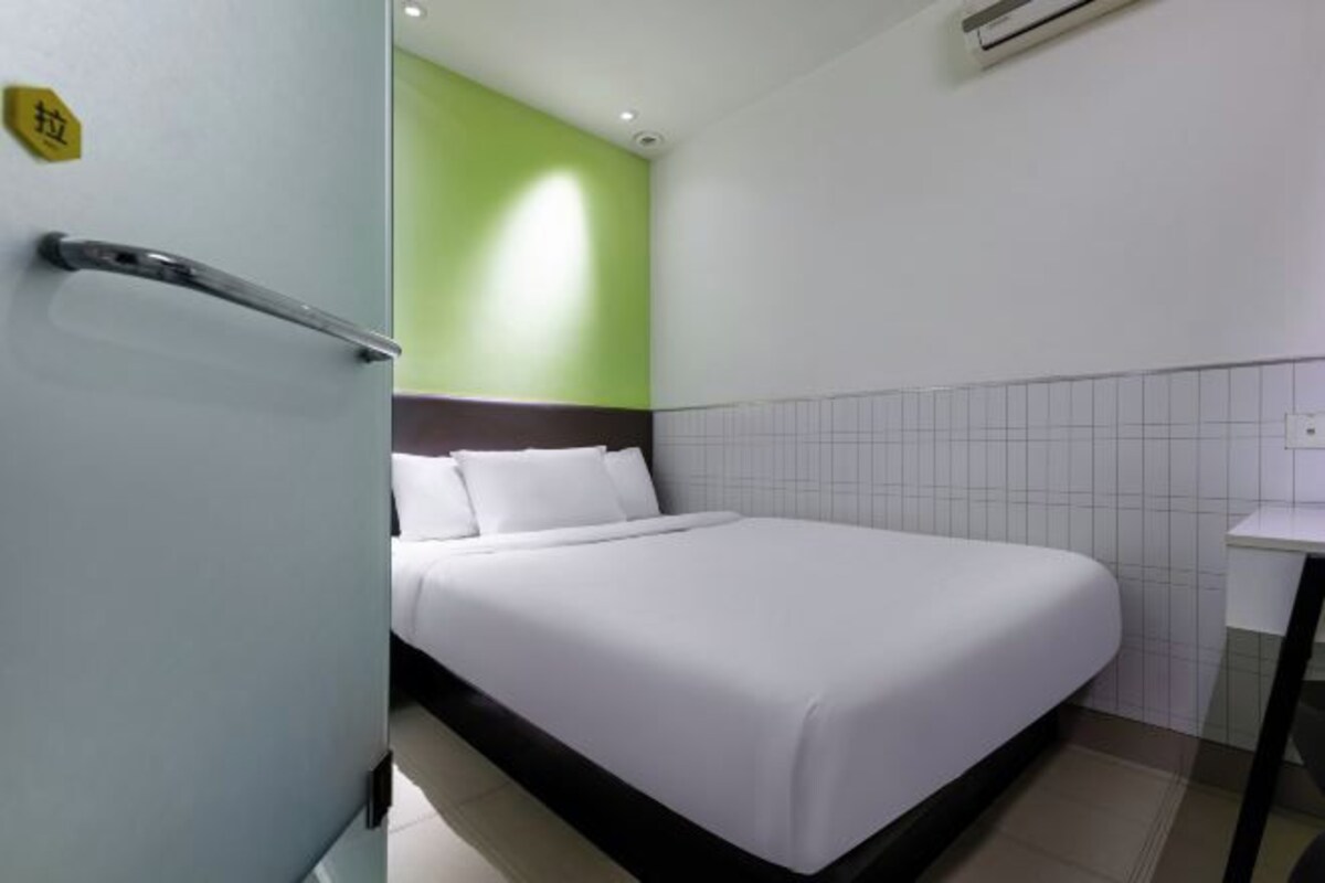 A hotel room with a bed, a white wall, a green accent wall, and a tiled floor.