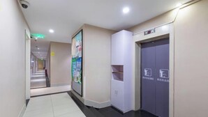 A hotel corridor with a tiled floor, a poster on the wall, a white cabinet, and an elevator with a sign. - 100 Inn (Shanghai Pudong Jinqiao) (Shanghai)