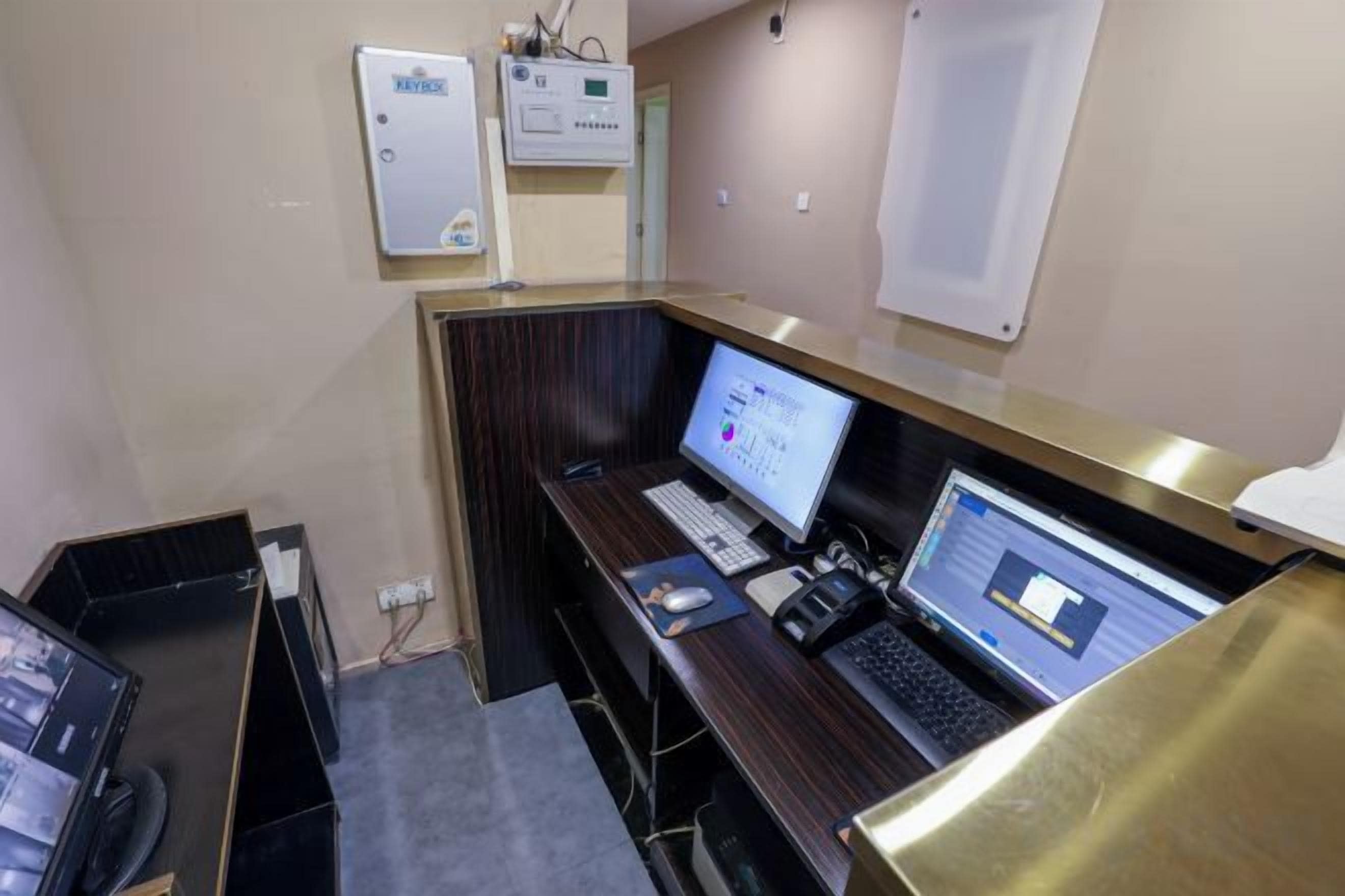 Quarto de hotel com escrivaninha, dois computadores, telefone e painel de controle fixado na parede.