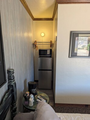 A compact room with a bed, a small table with toiletries, a microwave, and a refrigerator.
