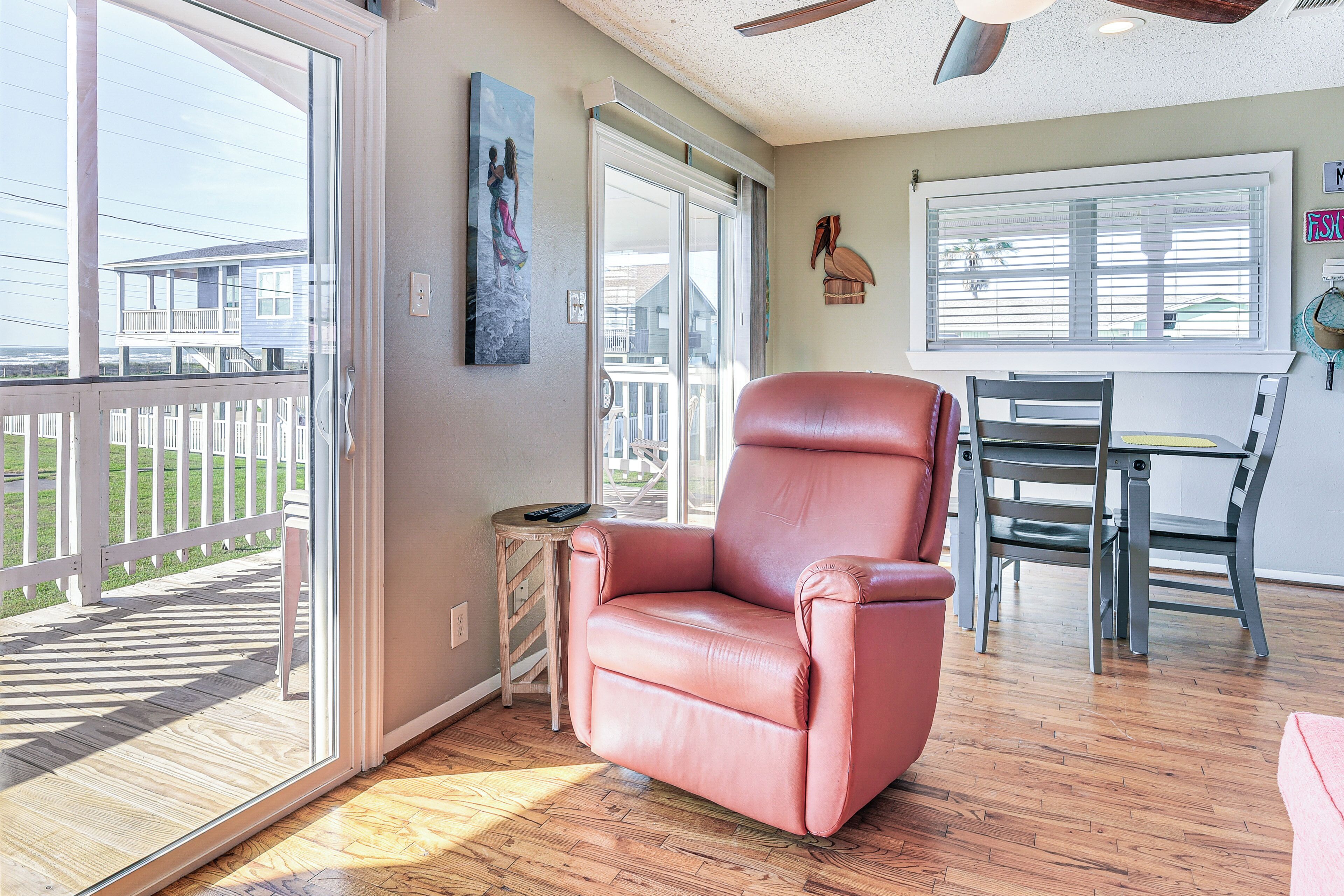 A room with a sliding glass door leading to a deck, a leather armchair, a dining table with chairs, and a ceiling fan.