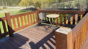 A wooden deck with a railing, two chairs, and a small round table.