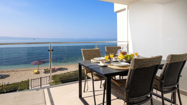 Un balcon avec une table préparée pour le petit-déjeuner, donnant sur une plage et la mer.