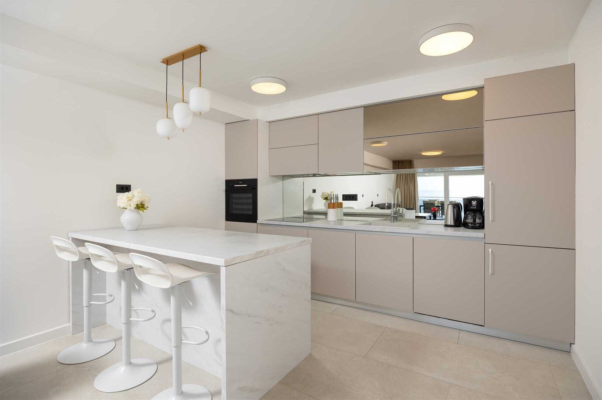 A modern kitchen with a marble island, white bar stools, and a view of the living area.