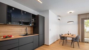 A modern kitchen with dark cabinetry, a wooden countertop, and a dining area with a table and chairs. - Paoma Middle Floor No.2 (Podstrana)