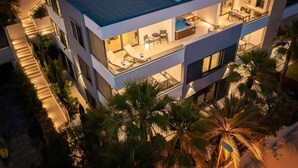 A modern multi-story building with a rooftop pool, outdoor seating, and a well-lit interior.