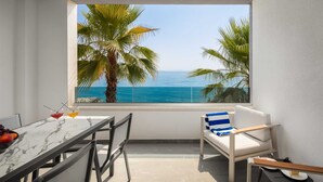 A balcony with a view of the sea, a table with drinks, and a chair with a striped cushion.