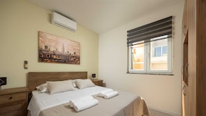 A bedroom with a bed, a nightstand, a bedside table, a window with blinds, and a cityscape painting on the wall. - Villa Beverly Hills, Heated pool, Jacuzzi, 12 people (Zadar)