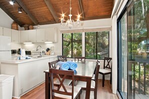 A modern kitchen with white cabinets, a dining table with chairs, and a large window with a view of greenery.