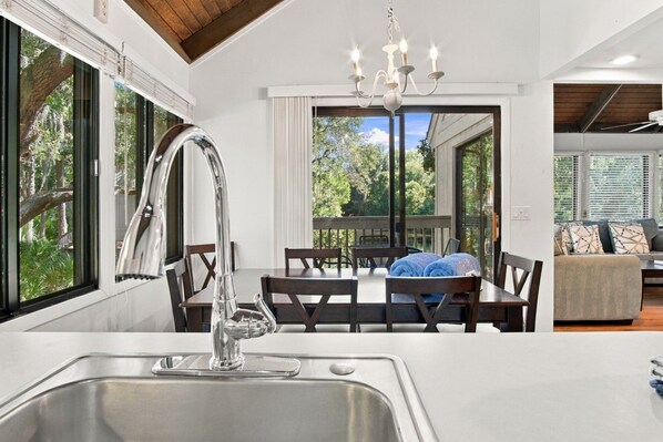 A modern kitchen with a stainless steel sink, a dining area with a table and chairs, and a chandelier.