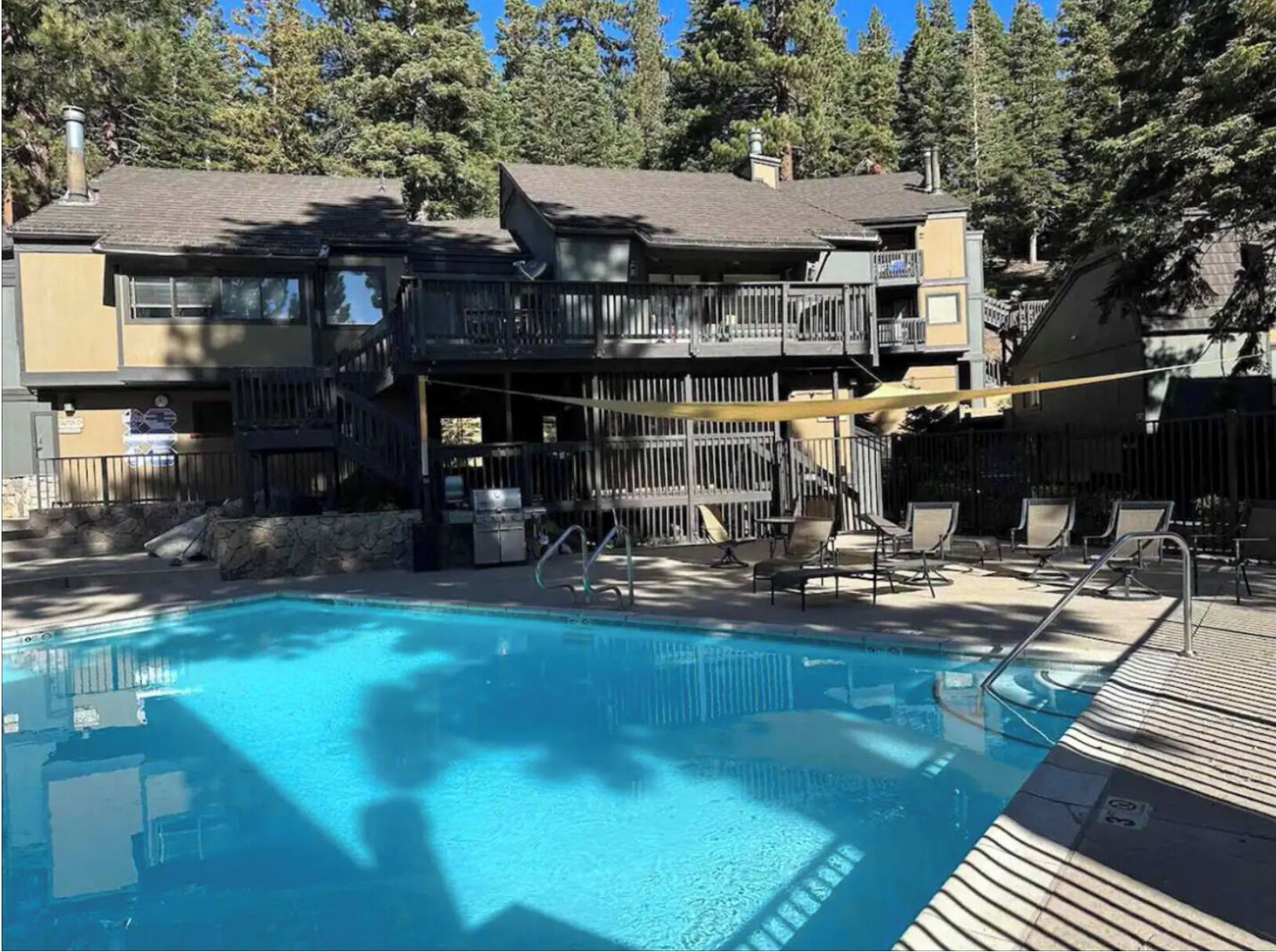A pool area with a wooden deck, lounge chairs, and a building with a balcony.