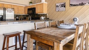 Une cuisine avec des meubles en bois, un réfrigérateur en acier inoxydable, un four à micro-ondes noir et un coin repas comprenant une table et des chaises en bois.