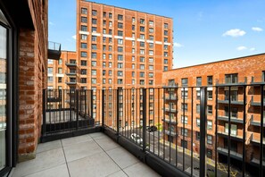 A balcony with a tiled floor, a black metal railing, and a view of a high-rise building with multiple windows and balconies. - Stylish 2 Bed Apartment - 2 Bathrooms - Balcony (West Midlands)