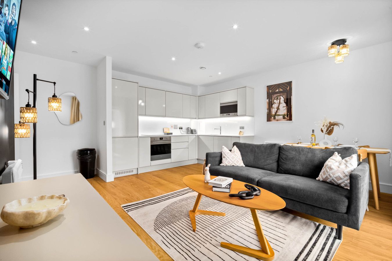 A modern living room with a grey sofa, wooden coffee table, and a kitchen in the background.