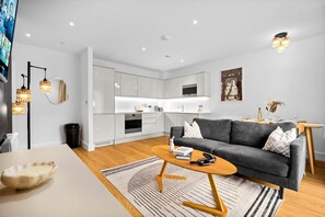A modern living room with a grey sofa, wooden coffee table, and a kitchen in the background. - Stylish 2 Bed Apartment - 2 Bathrooms - Balcony (West Midlands)