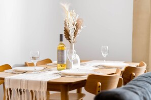 A dining table set with plates, cutlery, and a bottle of wine, surrounded by wooden chairs. - Stylish 2 Bed Apartment - 2 Bathrooms - Balcony (West Midlands)