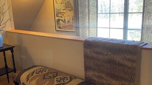 Ein Zimmer mit einer hölzernen Bank, einem gerahmten Bild an der Wand, einem Fenster mit Vorhängen und einer Deckenleuchte.