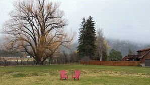 Ein grasbewachsener Garten mit zwei roten Stühlen, einem Holzzaun und einem großen Baum.