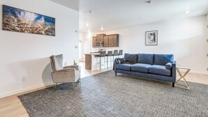 Un salon moderne avec un canapé bleu, un fauteuil gris et un grand tableau représentant un paysage urbain.
