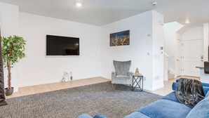 Un salon moderne avec un téléviseur à écran plat, un fauteuil gris, un canapé bleu et un tapis gris.