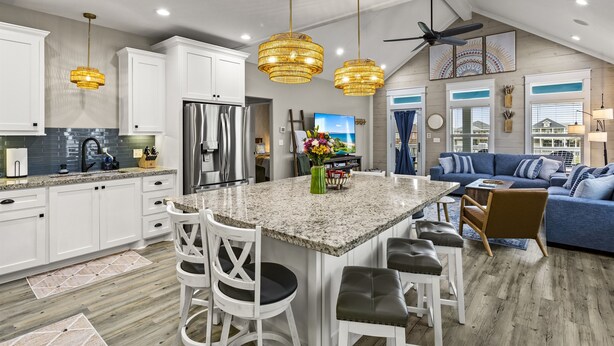 A spacious kitchen with white cabinets, a granite countertop, and a central island with seating. There is a ceiling fan and a large window providing natural light. - Family Friendly-Sleeps 10-BBQ-EV-Game Rm-Walk to Beach-Fire Table-Fully Stocked (Crystal Beach)
