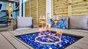 A fire pit with blue glass pebbles and two glasses of a beverage on a table. - Family Friendly-Sleeps 10-BBQ-EV-Game Rm-Walk to Beach-Fire Table-Fully Stocked (Crystal Beach)