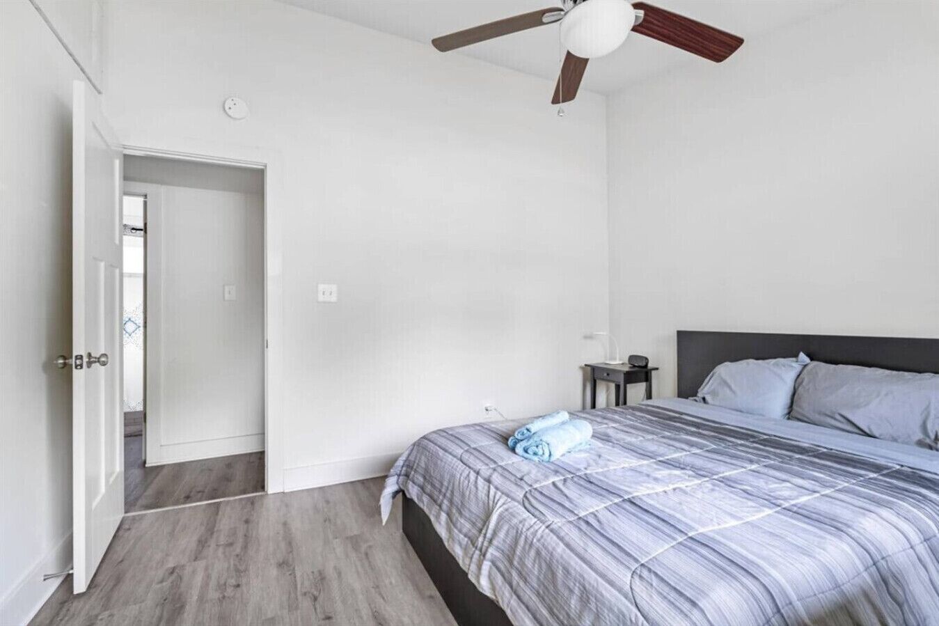 Une chambre à coucher comprenant un lit, un ventilateur de plafond, une table de chevet et une porte donnant sur une autre pièce.