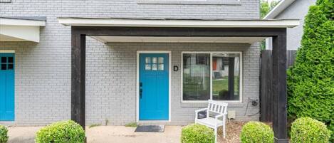 A two-story house with a blue door, a covered porch, and a white bench.