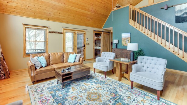 A spacious living room with a wooden ceiling, a staircase, and a large window. - 5 Mi to Cherokee Lake: Pet-Friendly Cabin w/ Deck! (Murphy)