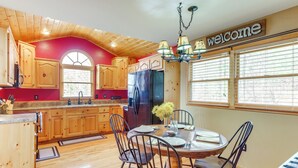 A kitchen with wooden cabinets, a black refrigerator, and a dining table set for four. - 5 Mi to Cherokee Lake: Pet-Friendly Cabin w/ Deck! (Murphy)