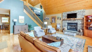 A spacious living room with a stone fireplace, leather sofa, and a staircase leading to an upper level. - 5 Mi to Cherokee Lake: Pet-Friendly Cabin w/ Deck! (Murphy)