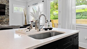 A modern kitchen with a large island, a stone accent wall, and a view of the outdoors. - Elegant Atlanta Home with Fireplace & Private Yard (Atlanta)