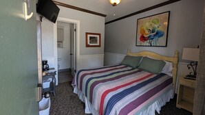 Een slaapkamer met een bed, een plafondventilator, een schilderij en een televisie aan de muur.
