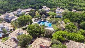 An aerial view of a residential area with multiple houses, a central swimming pool, and lush greenery. - Bz06 Casa com Piscina a 200M da praia (Buzios)