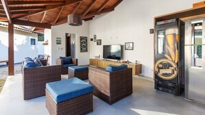 A covered outdoor seating area with wicker furniture and a large television screen. - Bz06 Casa com Piscina a 200M da praia (Buzios)