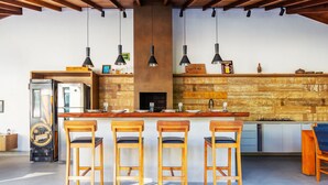 A modern kitchen with a central island, bar stools, pendant lights, and a rustic wooden wall. - Bz06 Casa com Piscina a 200M da praia (Buzios)