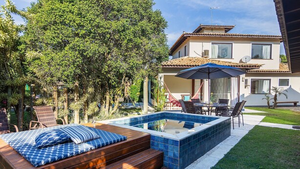 A backyard with a hot tub, wooden deck, and outdoor furniture. - Bz06 Casa com Piscina a 200M da praia (Buzios)