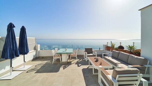 A terrace with a table and chairs, a sofa, and potted plants.