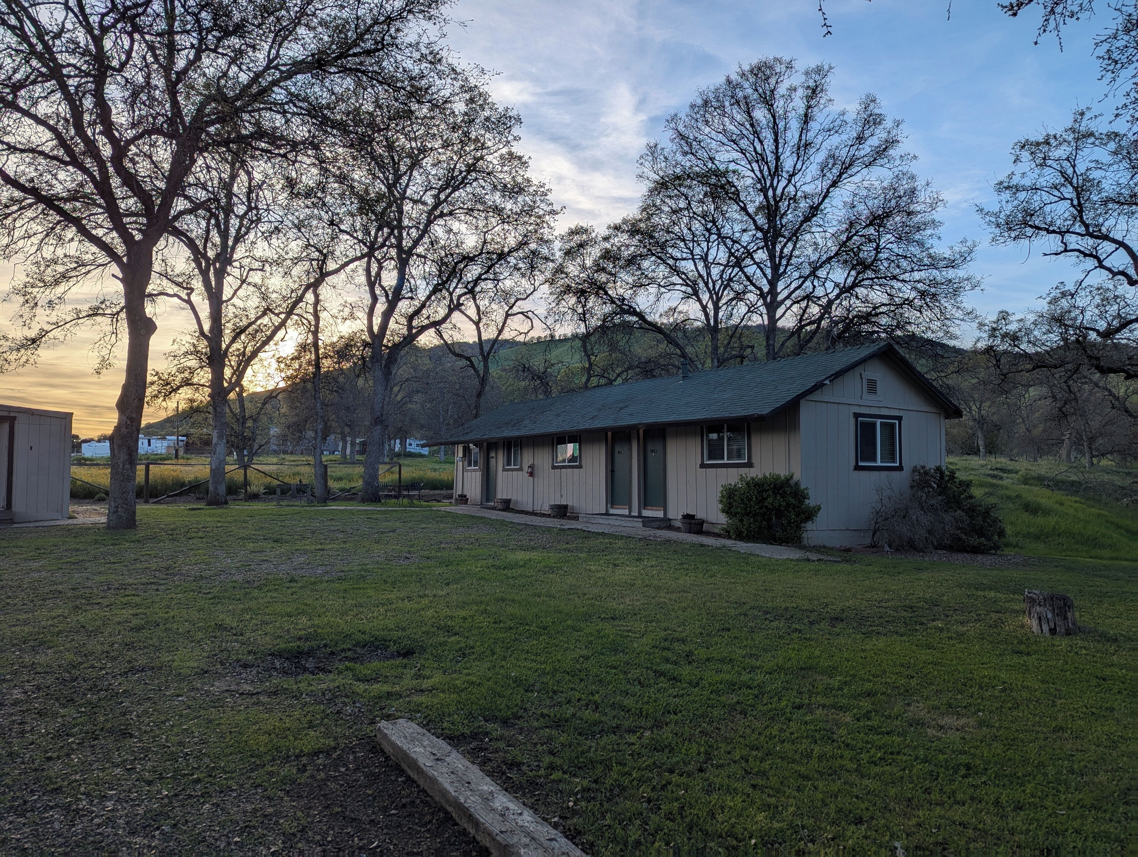 A small, single-story building with a green roof, surrounded by a grassy area and trees.